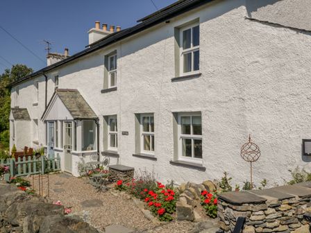 A white stone cottage with a pebble garden path and red flowers at 1 Sunny Point Cottages in Crook