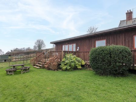 A wooden house with a small porch and stairs surrounded by bushes and a picnic table on a grassy lawn at The Willow Lodge near Lyme Regis
