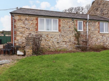 Stone cottage exterior with grass lawn and metal table and chairs at The Goathouse Cottage near Lyme Regis