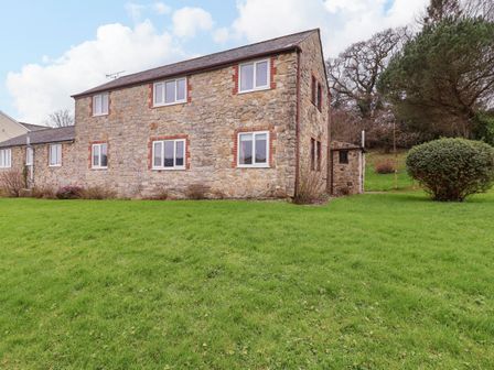 A stone house with white windows and a green lawn at The Hayloft Cottage Apartment near Lyme Regis
