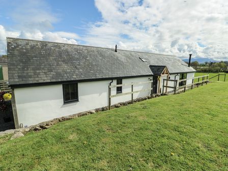 A single-story building with a slate roof and fenced grassy area at Ty Cuddfan in Llangoed