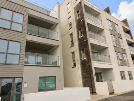 The exterior of a multi-story residential building with glass balconies and large windows at Crantock Reach in Newquay