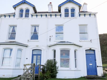 A white multi-story house with blue doors and window frames and a wooden fence in front at Carriguisnagh in Ballycastle