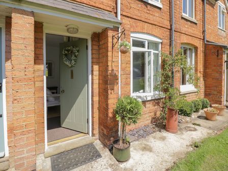 A brick house entrance with a partially open green door and potted plants outside at Meadow View in Banbury