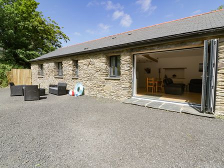 An outdoor seating area with chairs and a table next to a stone building with open doors showing an interior with chairs and a table at The Cart House in St Ewe near Sticker