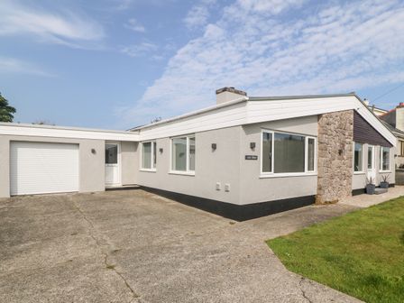 A single story house with a garage and driveway with a small grassy area at Little Mead in Trearddur Bay