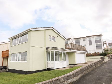 A two story house with multiple windows a porch a garage and a grass lawn at The Little Dolphins in Rhosneigr