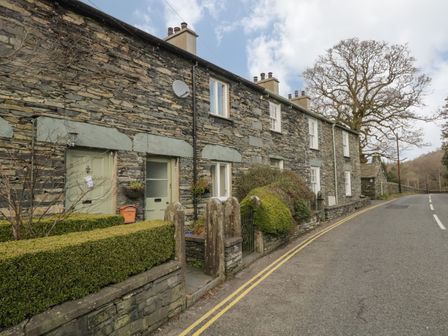 A row of stone cottages with green doors and trimmed hedges along a roadside at Oak Tree Cottage in Coniston