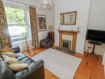 A living room with a black sofa and cushions a fireplace with a mirror above it a television on a stand and patterned curtains at Hawthorn House in Pembroke