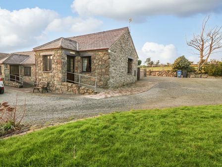 A stone cottage with a tiled roof and gravel driveway next to a grassy area at Trem Y Wyddfa in Gaerwen