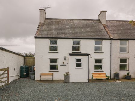 A white two-story house with two benches outside and gravel in front at Bron Gadair in Newborough