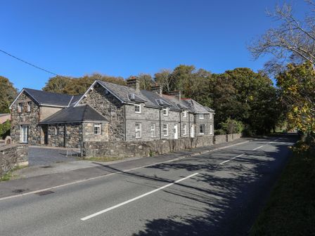A stone house next to a road with trees in the background at Gwynle - Llanystumdwy in Llanystumdwy near Criccieth
