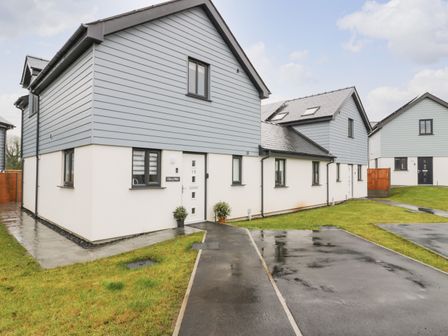 A cluster of modern semi detached houses with gray siding and white walls with parking spaces and grass at Can y Mor in Benllech