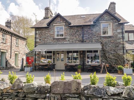 A stone building with outdoor seating and an awning reading freda and ray with plants in front at The Bakers Loft in Grasmere
