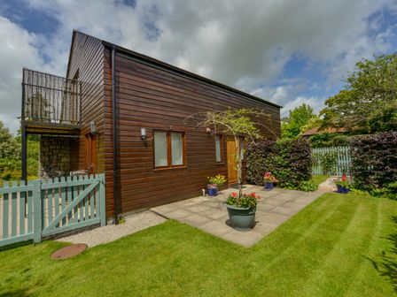 A wooden house with a patio and potted plants in a green garden at Cholwell Barn Apartment Mary Tavy