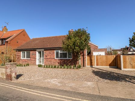 A single-story brick house with a tiled roof a gravel driveway and a tree in front at Sunnyside in Wells-Next-The-Sea