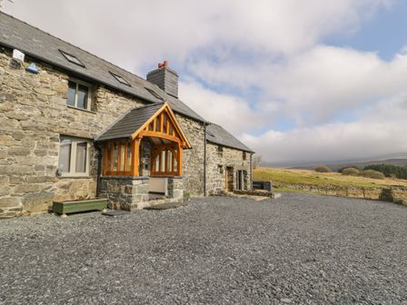 A stone house with a wooden porch and gravel driveway in a rural area at Hen Dy Craig Yr Ronwy Capel Celyn near Bala