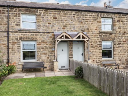 Stone house exterior with two white doors under wooden porch and two benches in front garden at Holida Hoose in Belford