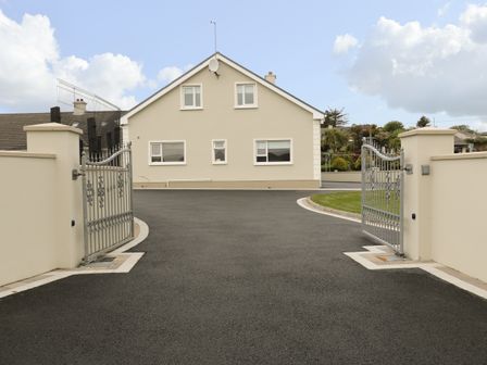 A driveway with open metal gates leading to a beige house with multiple windows at Loughanure Lake View in Loughanure County Donegal