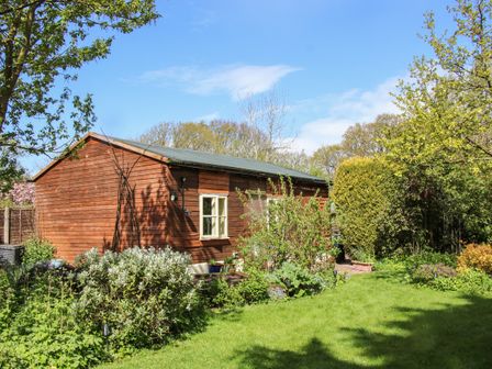 A garden with bushes grass and trees beside a wooden shed at The Garden Lodge in Upton Cressett near Bridgnorth