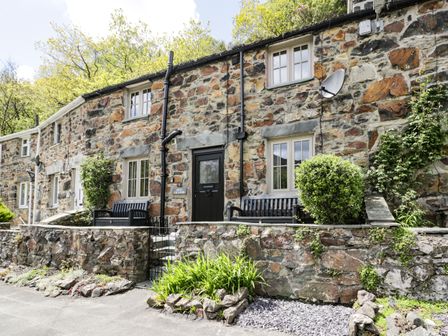 Exterior of a stone cottage with black doors and benches by the entrance at Swn yr Afon in Beddgelert