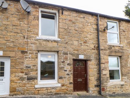 Stone exterior of a house with a brown door and white framed windows and two satellite dishes at Hunter Cottage in Haltwhistle near Hadrian's Wall