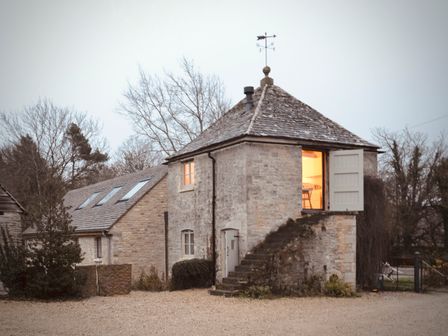 A stone building with external stairs and open upper door showing indoor light at High Cogges Farm Holiday Cottages - The Granary High Cogges near Witney