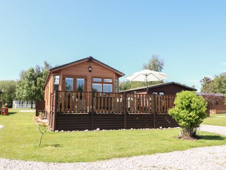 A wooden cabin with a deck and umbrella in a grassy area at Doormouse Lodge in South Lakeland Leisure Village