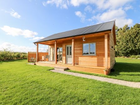 A wooden cabin with a porch, two chairs, a small table, and a grassy lawn at Rising Sun in Kirkbymoorside