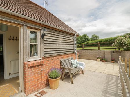 An outdoor patio with a wooden bench and potted plants beside a wooden and brick house wall at Holmer Farm in Pudleston near Leominster