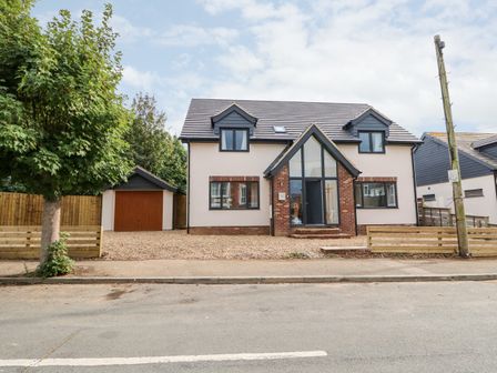 A two story house with a garage and a tree in front at The Glass House in Hunstanton