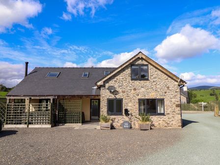 A stone house with black windows and a gravel driveway at Y Stabl The Stable in Llanrhaeadr-Ym-Mochnant