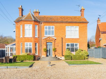 A front view of a red brick house with windows a blue door garden furniture on grass and gravel driveway at Sunnymeade in Buxton Norfolk