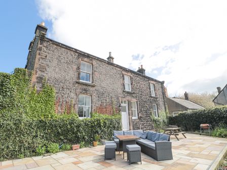 A stone house with ivy on the walls and a patio with outdoor seating and a picnic table at Jubilee House in Embleton
