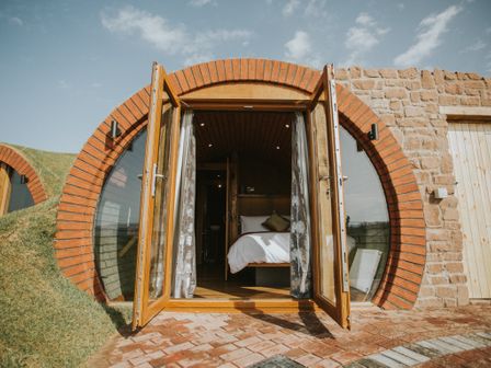 A bedroom with open wooden doors and circular brick frame at Otters View in Rhayader