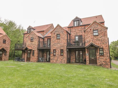 A brick apartment building with balconies and a grassy lawn at White Goose Cottage in Whitby