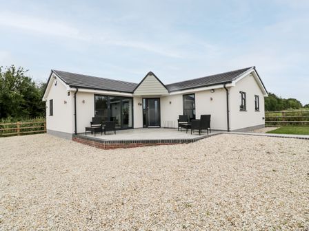 A single story white house with gray roof and patio furniture on a gravel yard at Strawberry Stables in Iwood near Congresbury