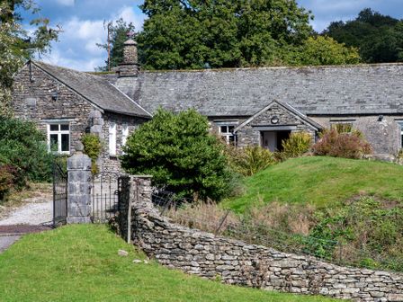A stone house with a slate roof behind a stone wall and a metal gate surrounded by greenery at Field Head House in Graythwaite near Hawkshead