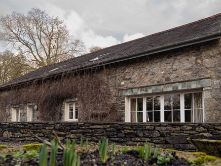 A stone building with windows and climbing plants by a stone wall at Bull Pen in Graythwaite near Hawkshead