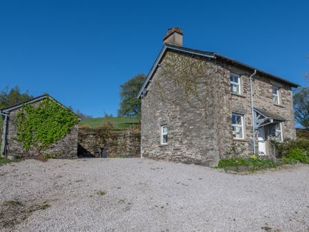 A stone cottage and an outbuilding with gravel driveway and plants at Eel House Cottage in Graythwaite Estate near Hawkshead