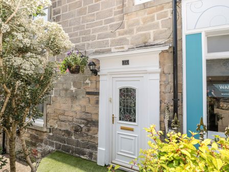A white door with stained glass and a hanging flower basket in front of a stone wall at 1A Chantry Place Morpeth