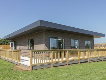 A single-story house with wooden exterior and railing on a lawn at Bluebell Wood in Brandesburton