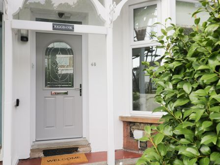 A front door with a welcome mat and a house number 48 next to a window with a bush nearby at Riggbank in Windermere