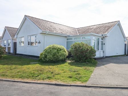 A white bungalow with a pitched roof and bushes in front at Glanaig in Morfa Bychan