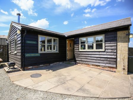 An exterior view of a single-story lodge with dark wooden siding and white-framed windows at Norton Cottage in Craven Arms