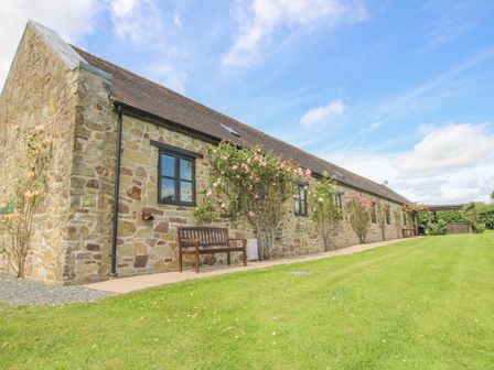 A stone exterior building with black framed windows a wooden bench and climbing roses on a lawn at The Park in Onibury near Craven Arms