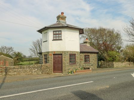 A stone and white two-story house with a brown door and windows alongside a road at Old Tollgate in Gwalchmai near Llangefni