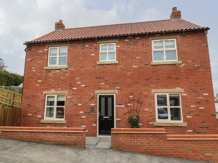 A brick house with a black door and six windows with a small brick wall in front at Holly Farm Cottage in Buckton And Bempton