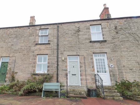 A stone exterior of a terraced house with two white doors and multiple windows at Lavender Cottage in Glanton