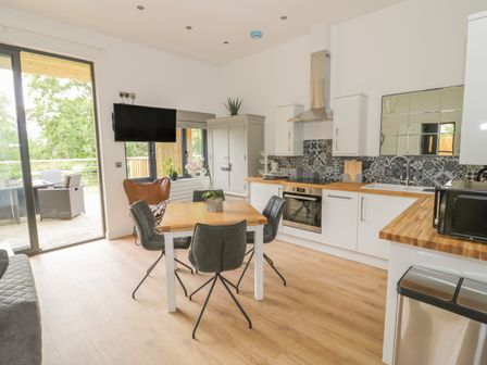 A kitchen and dining area with a wooden table and chairs a wall-mounted tv and sliding glass doors leading outside at The Leat in Droitwich Spa